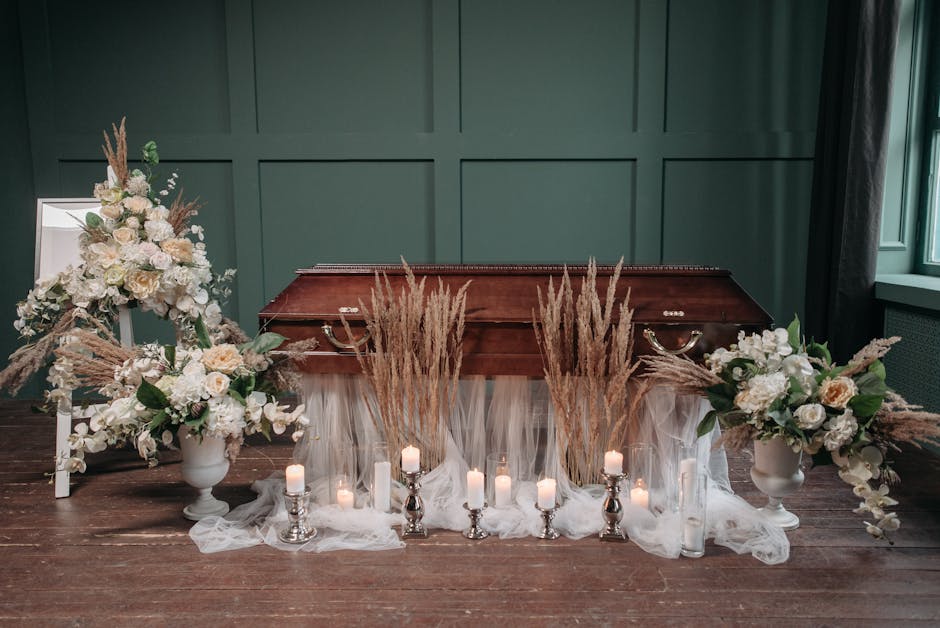 A funeral floral arrangement featuring two large white vases filled with white roses, peonies, and hydrangeas accented with green foliage, positioned symmetrically on either side of a vintage wooden c